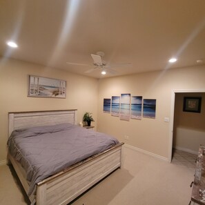 Ein Schlafzimmer mit einem Bett, einem Deckenventilator, einem Nachttisch mit Pflanze und einer Tür zu einem anderen Raum.