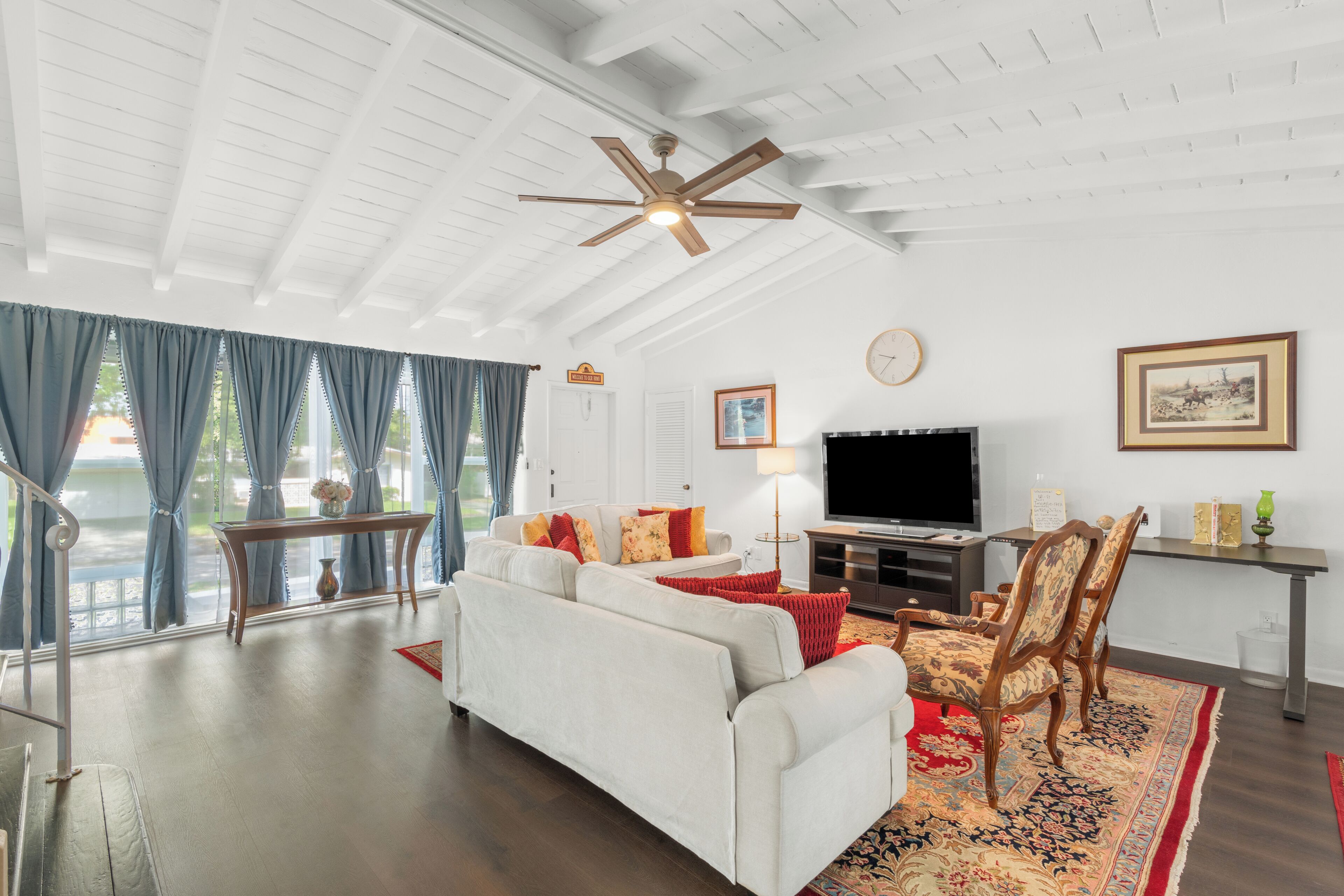 A spacious living room with a white sofa, a television, and a ceiling fan.