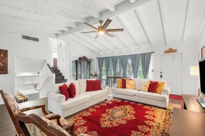 Ein geräumiges Wohnzimmer mit hoher Decke, weißen Wänden, einem roten Teppich mit Muster und einem weißen Sofa mit roten und gelben Kissen.