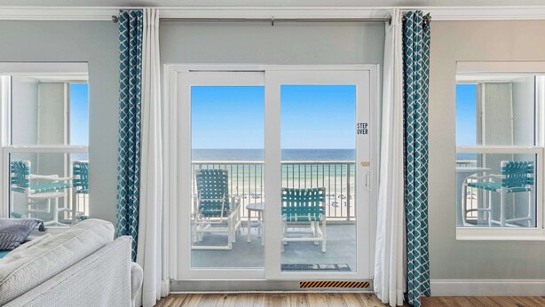 Quarto com vista para a praia, porta de correr de vidro e varanda com cadeiras.