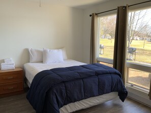A bedroom with a bed, a wooden nightstand, and a window with curtains.