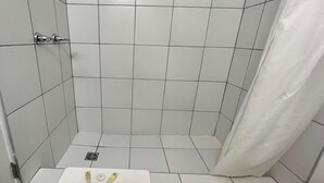 A small, tiled shower room with a white towel on the floor and a shower curtain. - Sunrise 5 Studio 2 Queens (Huntsville)