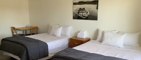 Habitación de hotel con dos camas, un escritorio, una silla, una mesita de noche y un ventilador de techo.