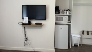 A room with a flat-screen TV mounted on the wall, a small refrigerator, a microwave, and a coffee maker on a shelf. - Sunrise 5 Studio 2 Queens (Huntsville)
