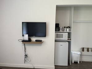 A room with a flat-screen TV mounted on the wall, a small refrigerator, a microwave, and a coffee maker on a shelf. - Sunrise 5 Studio 2 Queens (Huntsville)