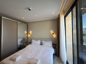 Ein Hotelzimmer mit einem großen Bett, Nachttischlampen, einem Spiegel und Blick auf die Stadt.