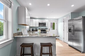 Eine moderne Küche mit weißen Schränken, einem Edelstahlkühlschrank, Granit Arbeitsplatten und zwei Holzhockern.