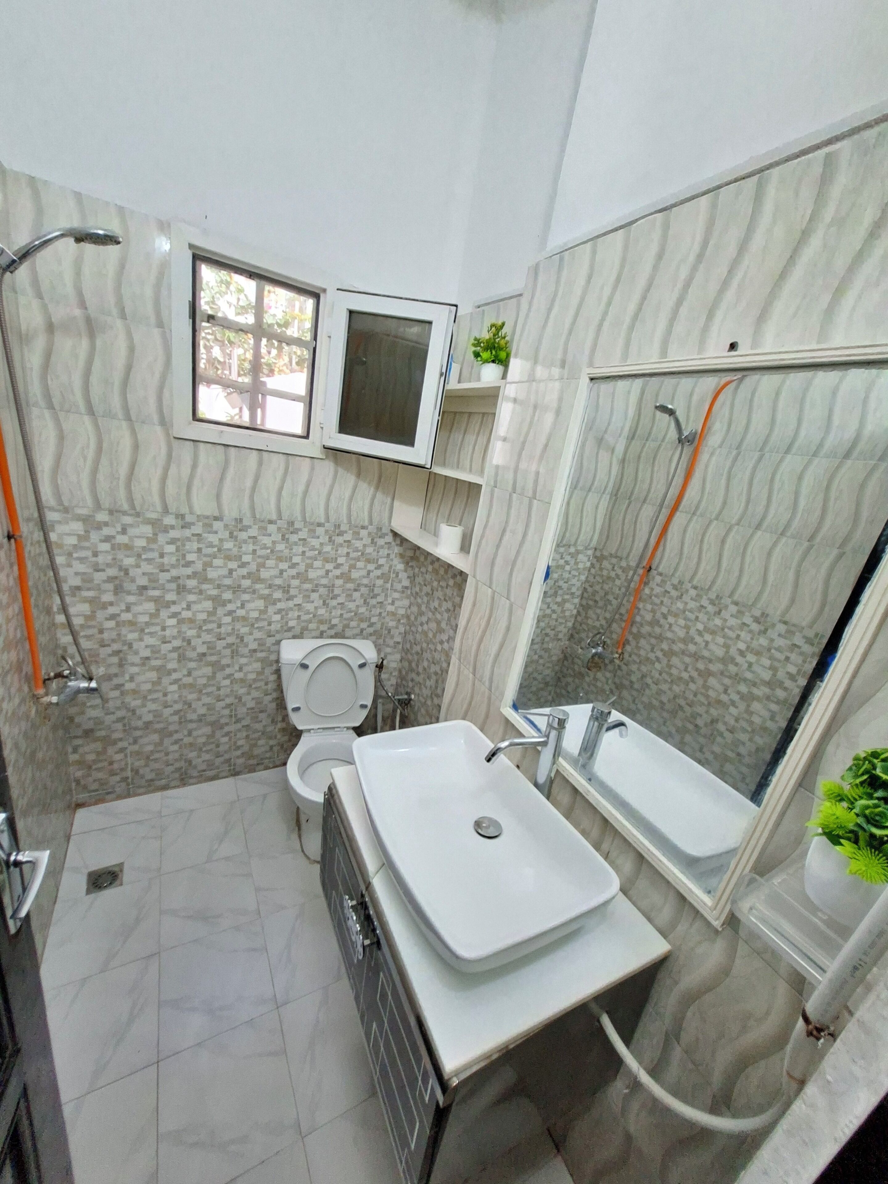 A bathroom with a toilet, sink, shower, and a window.