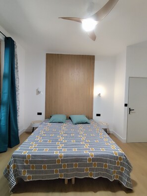 A bedroom with a bed, two pillows, a ceiling fan, a nightstand, a lamp, and a door.