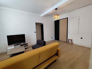 A modern living room with a flat-screen TV, a sofa, a small table, and a hanging light fixture.