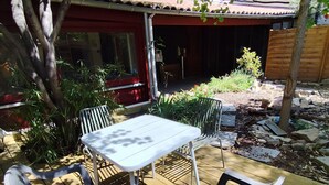 Eine Terrasse mit Tisch und Stühlen, umgeben von Grünpflanzen und einem Gebäude im Hintergrund.