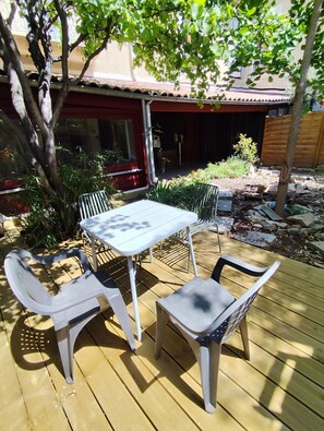Une terrasse avec une table et des chaises, entourée de verdure et avec un bùtiment en arriÚre-plan.