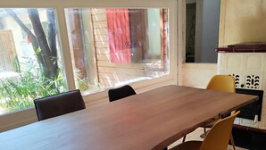 Ein Essbereich mit einem langen Holztisch, schwarzen und gelben Stühlen und Blick ins Freie durch große Fenster.
