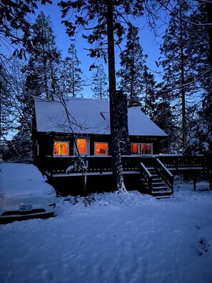 Eine Holzhütte mit schneebedecktem Dach, einer sichtbaren Treppe und Fenstern, die ein warmes Licht von innen werfen.