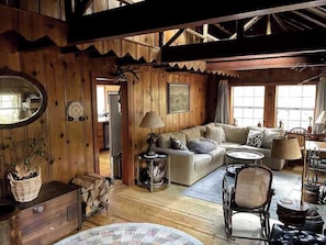 Ein gemütliches Blockhaus-Interieur mit Holzbalkendecke, einer Couch, einem Esstisch und einem Kamin.