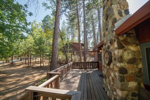 Une terrasse en bois avec un mur en pierre, entourée de grands arbres.