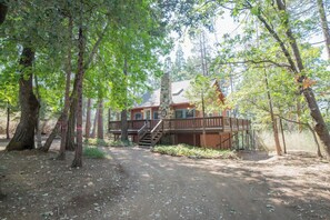 Een chalet met een houten terras, omringd door bomen.