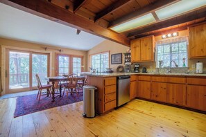 A spacious kitchen with wooden cabinets, a dining area with a table and chairs, and large windows allowing natural light. - Daisy’s Place | Cozy Twain Harte Cabin w/ Twain Harte Lake Access (Twain Harte)