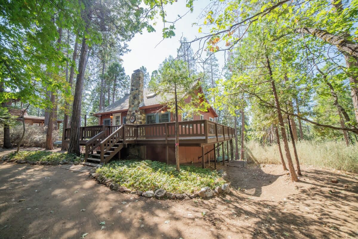 A cabin with a deck, surrounded by trees and a dirt path.