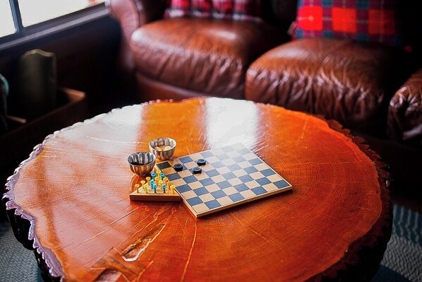 A wooden coffee table with a chessboard and pieces, a metal bowl, and a small cup.