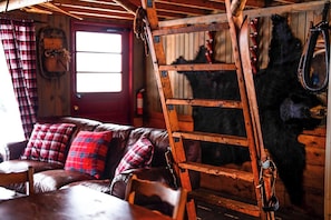 A rustic interior with a wooden ladder, a leather couch with plaid pillows, and a bear mounted on the wall.