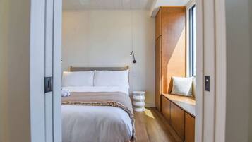 A bedroom with a bed, bedside table, lamp, and a window with a view.