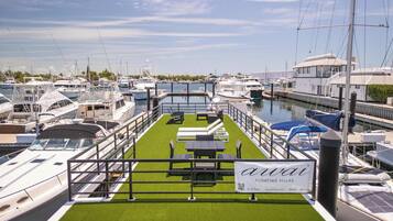 A marina with boats docked, a floating villa with a green deck and lounge chairs, and a sign advertising 'AwaVi' floating villas.