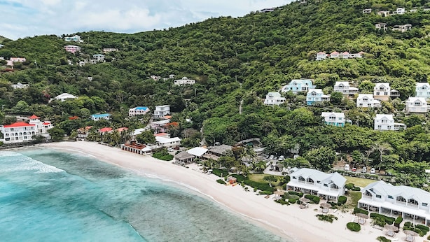 Zona costera con playa, casas y abundante vegetación.