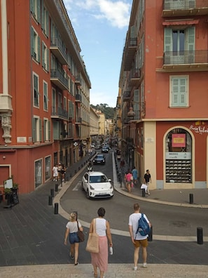 Una calle con edificios, un coche blanco y gente caminando.