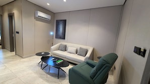 En moderne stue med en sofa, en grøn lænestol, et sofabord og en aircondition-enhed på væggen.