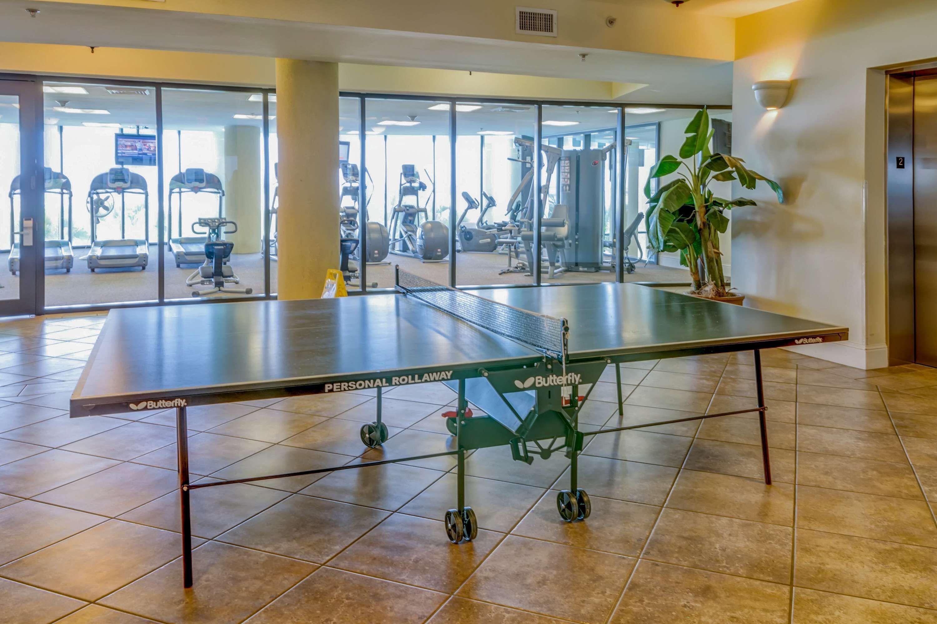 Una mesa de ping pong en un gimnasio, con equipo de ejercicio al fondo.