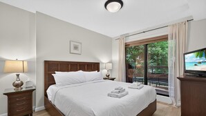 Habitación de hotel con una cama grande, televisión, mesita de noche con lámpara y vistas a un balcón con cortinas.