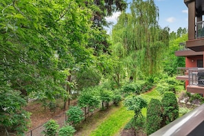 A lush garden with a variety of trees and shrubs, a clear pathway, and a modern building with a balcony. - Spacious 3 Bd at Playa 220! Pool, 1 Min To Beach! (Kelowna)