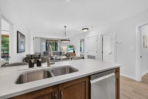 A modern kitchen with a central island, stainless steel appliances, and a view to the living area. - Spacious 3 Bd at Playa 220! Pool, 1 Min To Beach! (Kelowna)