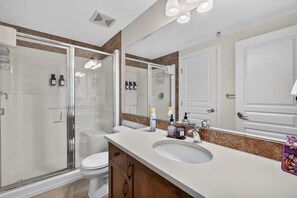 Un bagno moderno con cabina doccia in vetro, un water, un lavabo con specchio e articoli da toilette sul ripiano.