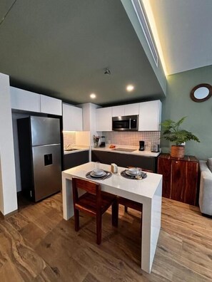 A modern kitchen with white cabinetry, a built-in oven, and a dining area with a white table and chairs. - Sensai Downtown by Riviera Maya Suites  (Playa del Carmen)