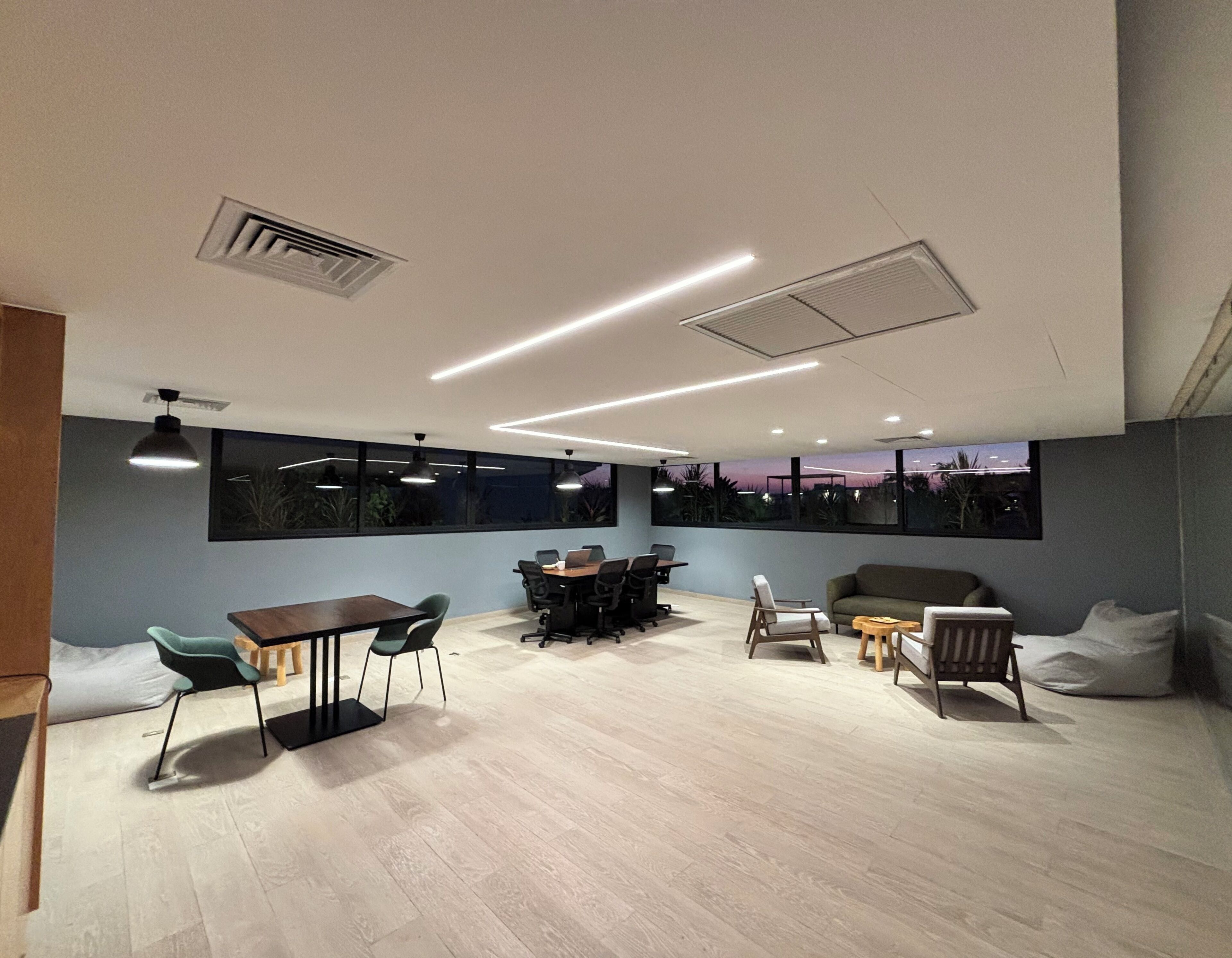 Una sala riunioni moderna con un tavolo grande, sedie e un divano. Sono presenti ampie finestre con vista sull'esterno.