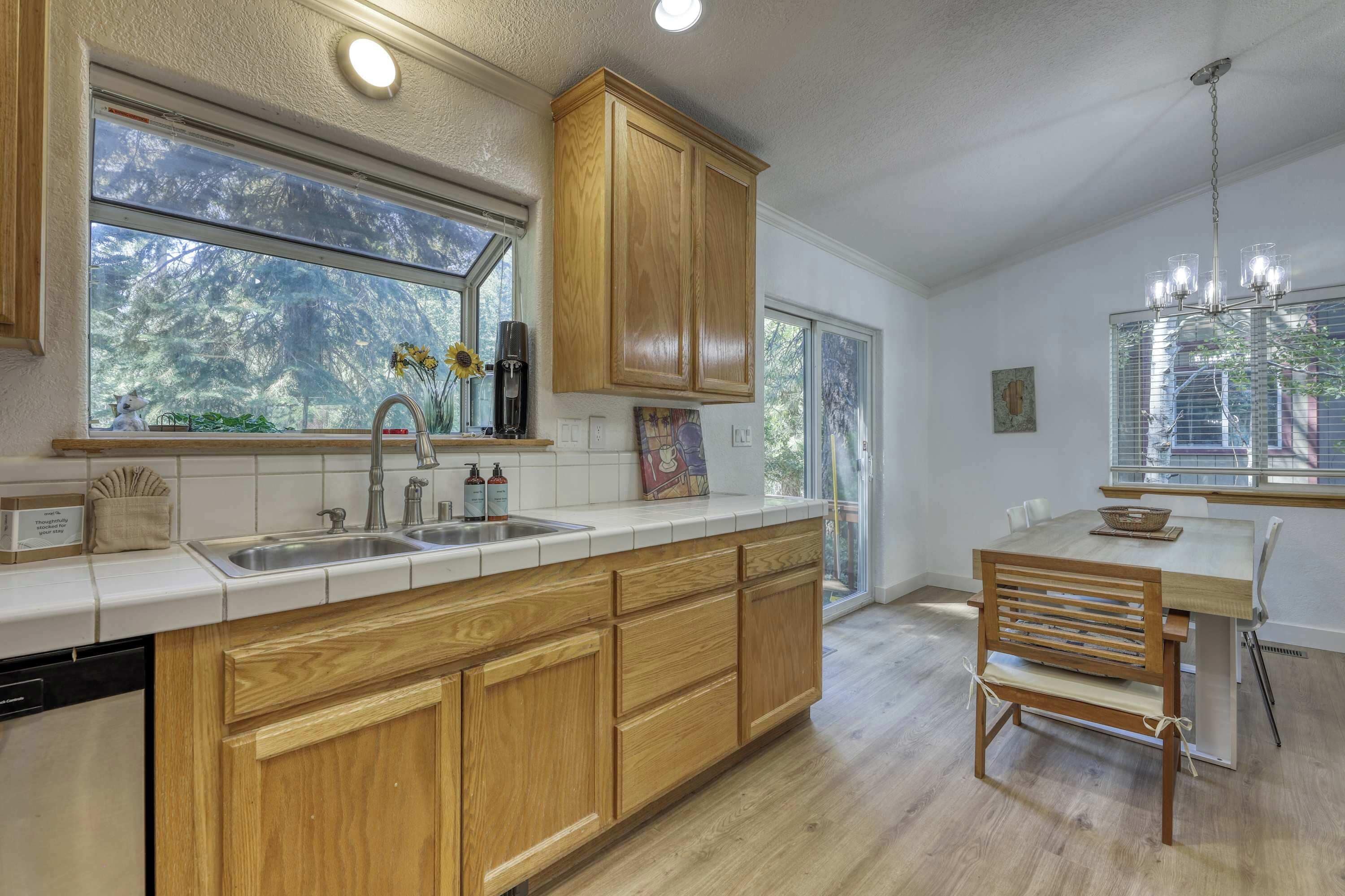A modern kitchen with wooden cabinets, a large window, and a dining area with a wooden bench.