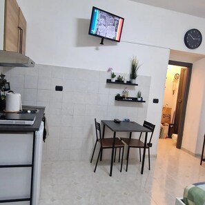 A kitchen with a TV, a dining table with chairs, a clock, and a hallway with a door. - Tranquility and comfort near Trastevere (Roma)