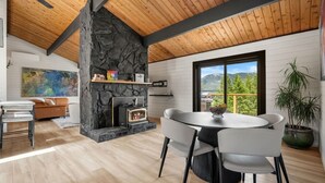 Ein modernes Interieur mit Kamin aus Stein, einem runden Esstisch und Blick auf Berge durch ein großes Fenster.