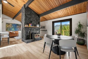 Un interior moderno con una chimenea de piedra, una mesa redonda para comer y vistas a las montañas a través de un ventanal grande.