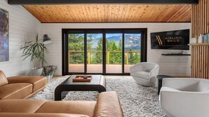 Ein modernes Wohnzimmer mit Holzboden, großen Schiebeglastüren zu einer Terrasse und einem flachbildfernseher an der Wand.