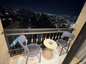 Varanda com duas cadeiras e uma mesa pequena, com vista para a cidade à noite.