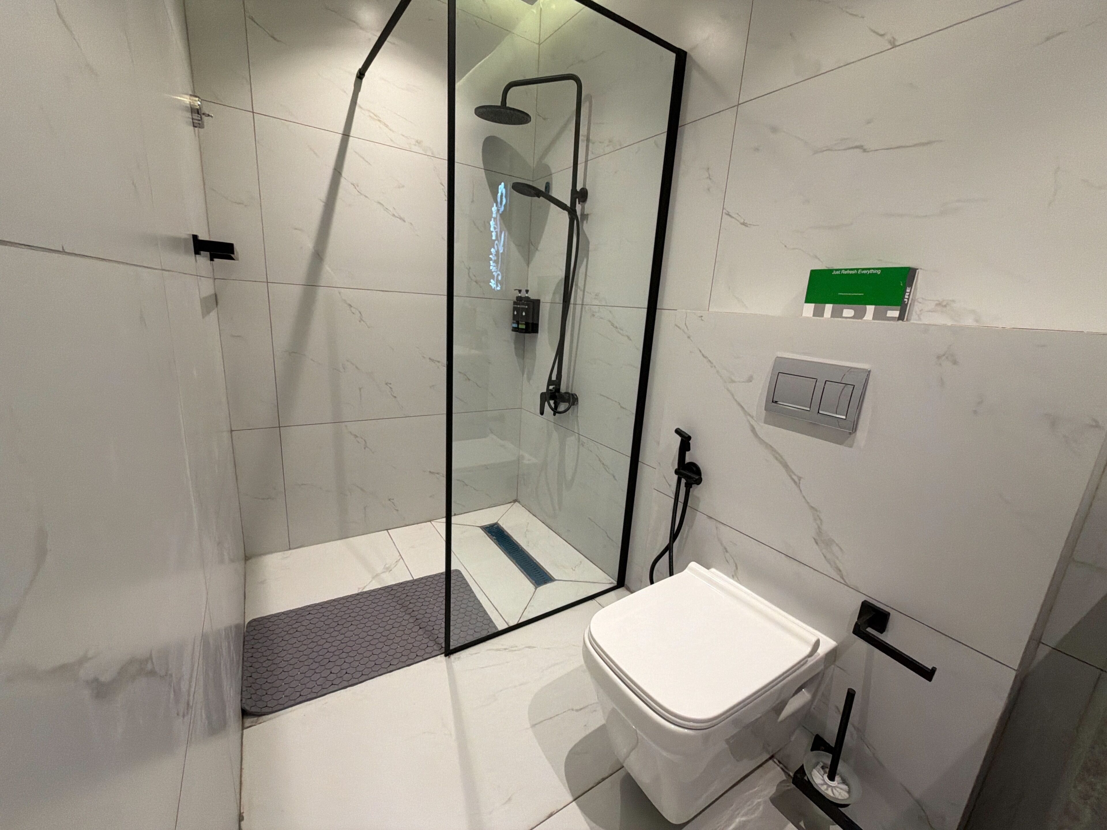 Un bagno moderno con doccia vetrata, un water e un piccolo portasapone verde.