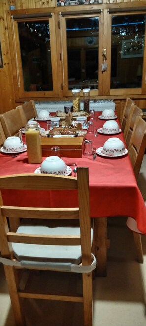 Une table à manger en bois, dressée avec de l’argenterie blanche et recouverte d’une nappe rouge, entourée de chaises en bois.