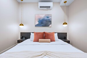 Una habitación de hotel con cama, dos mesitas de noche, aire acondicionado y una obra de arte colgada en la pared.