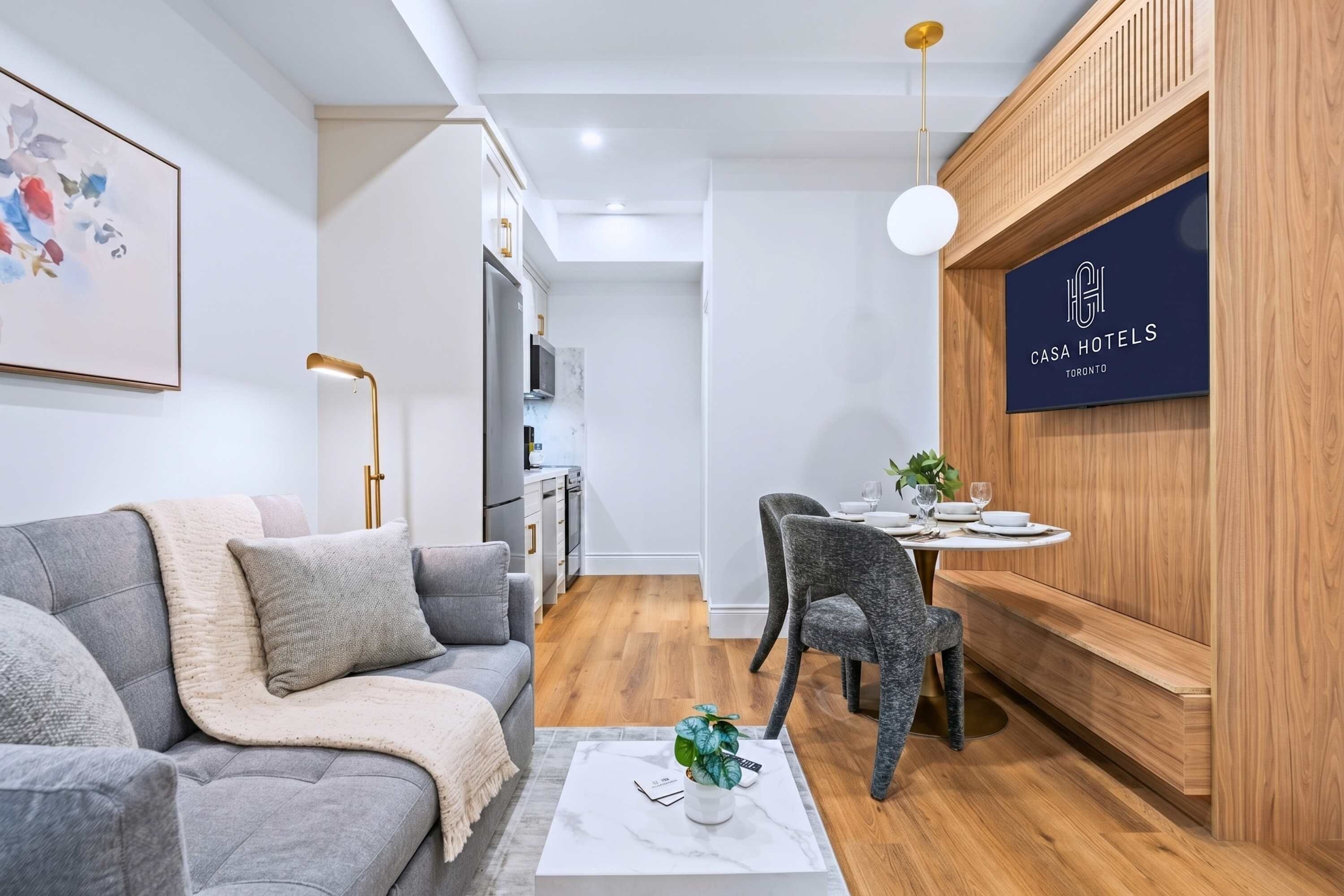 Een moderne hotelkamer met een grijze bank, een eettafel met stoelen, een houten accentmuur en een plafondlamp.