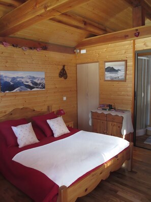 Une chambre dans une cabane en bois, avec un lit, deux oreillers, une commode, un miroir et deux tableaux encadrés accrochés au mur.
