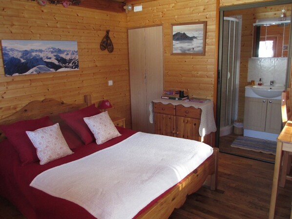Une chambre à coucher située dans une cabane en bois, comprenant un lit, des oreillers, une table de chevet, une commode et une salle de bain avec un lavabo et un miroir.