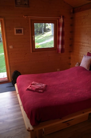 Una habitación de cabaña de madera con una cama, una ventana y una puerta que da al exterior.